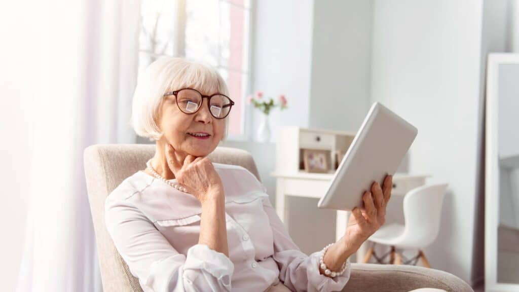 An older woman wearing glasses is intently using a tablet